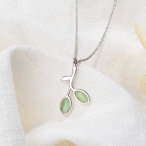 Detail of silver leaf necklace with green gemstones on white textured background