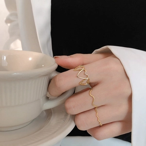 Minimalist gold heart cutout and wave ring set styled on hand with a coffee cup