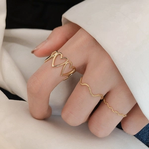 Three-piece gold hollow heart ring set and wavy thin bands worn as stacked rings