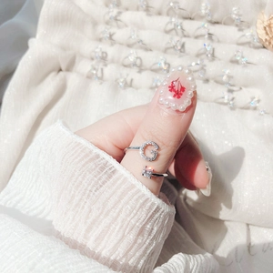 Detail of adjustable silver ring with letter G design and square gemstone on finger