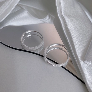 Pair of adjustable sparkling silver rings with frosted finish on reflective surface