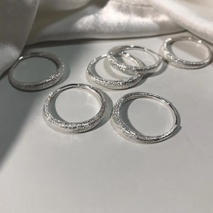 Set of six shimmering silver hoop earrings with a matte textured finish on white silk