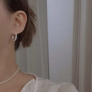 Close-up of sparkling silver hoop earrings with pavé stones and a pearl necklace