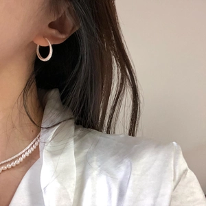 Close-up of textured silver hoop earrings paired with a white pearl necklace on a model