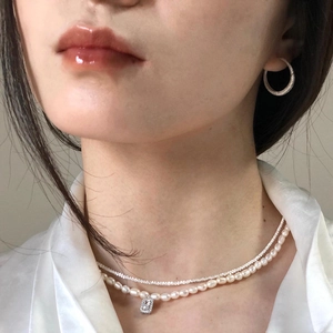 Detail of layered pearl necklace and shimmering silver pendant on elegant model