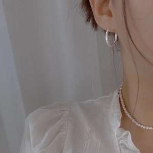 Close-up of sparkling textured hoop earrings and delicate white pearl necklace on model