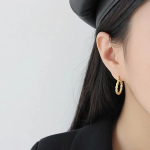 Elegant gold twisted rope hoop earrings worn by a model in a minimalist portrait