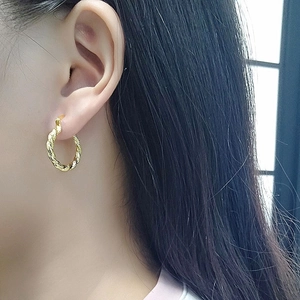 Close-up of golden twisted rope hoop earrings worn on a model's ear for detail
