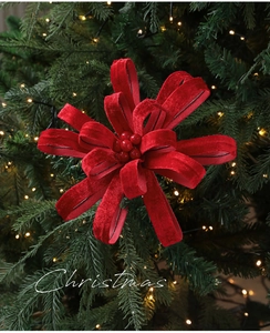 Close-up of red velvet Christmas flower ornament with berries on a glowing Xmas tree