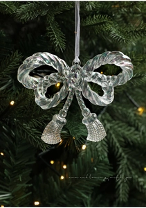 Close-up of iridescent acrylic bow ornament with tassels on a lit Christmas tree