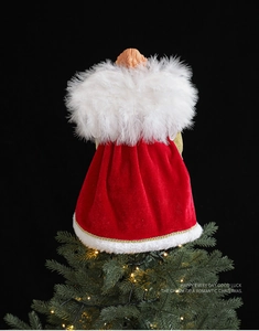 Detail of angel tree topper with red velvet robe and white feathery wings on pine