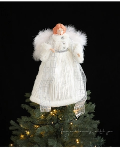 Close-up of white angel tree topper with feather wings on a glowing Christmas tree