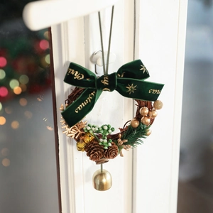 Couronne de Noël avec nœud en velours vert, pommes de pin et cloches dorées sur porte