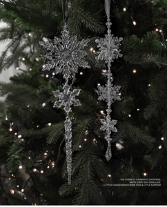 Detail von klaren Acryl Schneeflocken und Eiszapfen Anhängern an einem Weihnachtsbaum mit Licht
