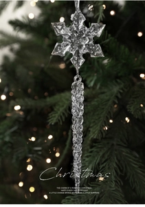 Nahaufnahme von Acryl-Schneeflocke und Eiszapfen-Anhänger am Weihnachtsbaum mit warmem Bokeh