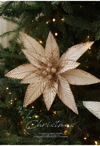 Detail of glittery champagne gold artificial flower ornament on a lit Christmas tree