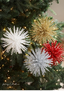 Close-up of glittery starburst ornaments in gold, silver and red on a lighted Christmas tree
