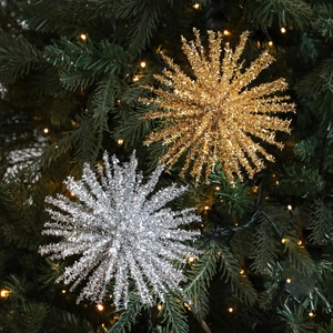 Glittery gold and silver starburst Christmas tree ornaments on a festive pine branch