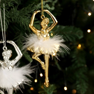 Golden ballet dancer Christmas ornament with white feathers hanging on a lit Xmas tree