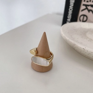 Détail d'une bague dorée avec nacre blanche sur un support en bois au design minimaliste