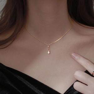 Close-up of a pear-cut zircon teardrop pendant on a gold chain over a woman's collarbone