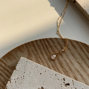 Macro detail of gold teardrop necklace with pear-cut zircon pendant on wooden stand