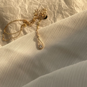Detail of gold water drop necklace with clear zircon pendant on aesthetic background