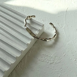 S925 silver irregular wave bangle with organic polished texture on white plaster stand
