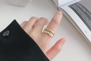 Detail of layered gold open ring with irregular lines worn against a minimalist backdrop