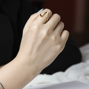 Close-up of a minimalist gold wave ring on a finger showing mirror-polished texture