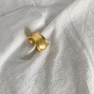 Macro shot of wide irregular wavy gold ring with matte texture on white fabric