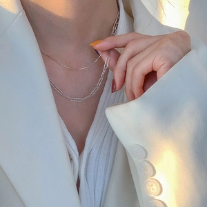 Close-up of layered silver snake and textured oval link necklaces on female model