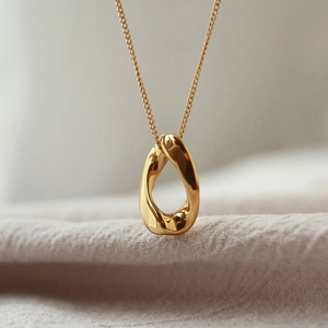 Close-up of a golden minimalist twisted teardrop pendant on a delicate cable chain