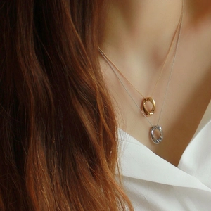 Close-up of layered gold and silver twisted oval pendant necklace on a white shirt