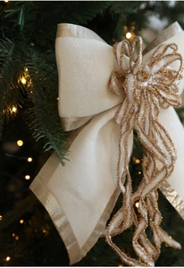 Close-up of cream bow ornament with gold glitter edges on a blurred Christmas tree