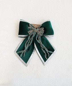 Close-up of velvet Christmas bow with silver trim and gold tassel on white plush background