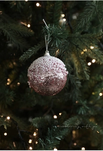 Détail d'une boule de Noël rose pailletée avec perles blanches sur un sapin de fête
