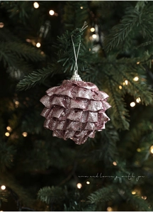 Détail d'une pomme de pin rose pailletée suspendue sur un sapin avec bokeh chaleureux
