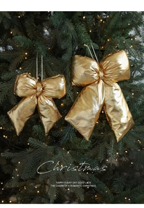 Golden glittering Christmas bow ornaments with strings hanging on a warm lit pine tree
