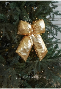 Close-up of a large shimmering gold Christmas bow hanging on a warm lit festive tree