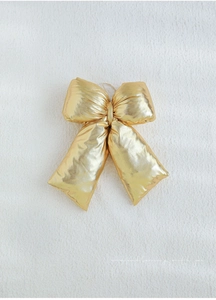 Close-up of a large gold metallic Christmas bow with shimmering texture and hanging loop