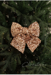 Detail einer roségoldenen Pailletten-Weihnachtsschleife an einem grünen Tannenzweig
