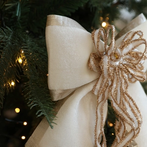 Cream satin Christmas bow ornament with gold glitter accents on a green tree branch