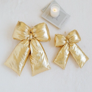 Golden Christmas bow ornaments with metallic finish on white faux fur background