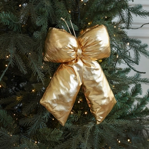 Golden glittering Christmas bow ornament hanging on a festive tree with warm lights