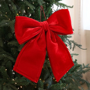 Large red velvet Christmas bow ornament hanging on a green Christmas tree with warm lights