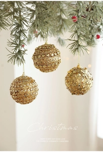 Detailed view of three golden Christmas ornaments with glitter and sequins hanging on a pine branch