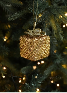 Close-up of golden glitter gift box ornament with bow on a glowing Christmas tree