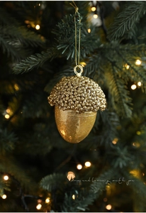 Detailed view of golden acorn ornament with glitter and beads on a green Christmas tree