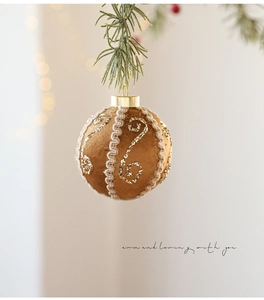 Brown fabric Christmas ball with gold glitter swirls and lace on a pine branch